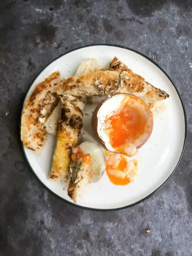 Hard-boiled eggs sliced lengthwise showing firm yellow centers, arranged on wooden cutting board with fresh herbs